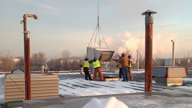 Crew in safety vests guiding a helicopter-lifted rooftop unit onto its curb