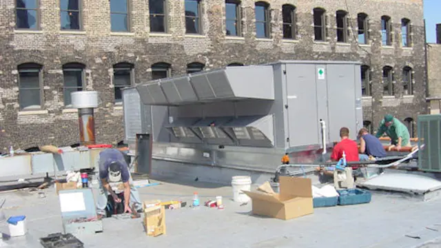 Technicians working beside a large rooftop air handling unit on a downtown Chicago building
